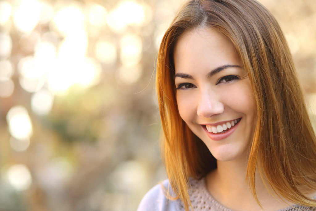 A close up headshot of a beautiful Asian woman smiling outdoors.