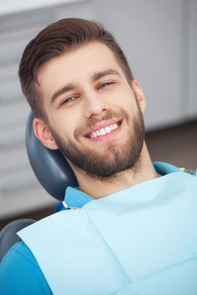 An image of a happy male dental patient sitting in a dental chair.