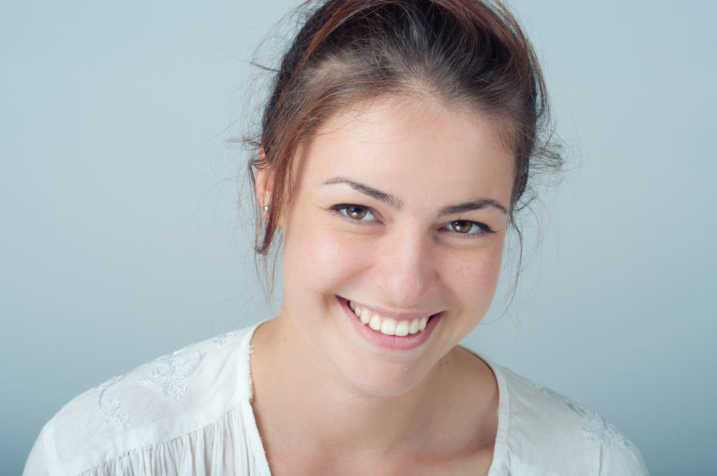 Young attractive female with white teeth smiling against a blue background