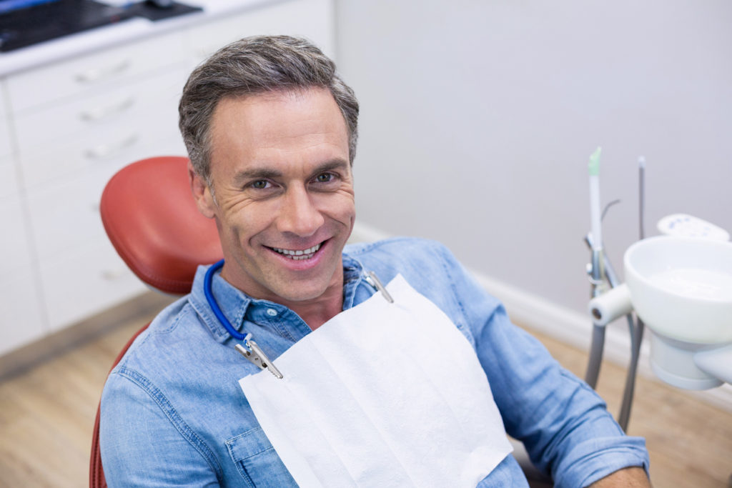 Middle aged male patient smiling in a dentists chair