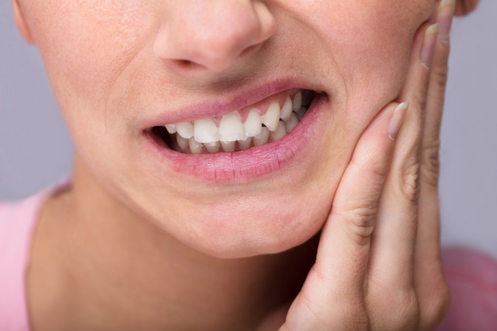 Woman holding her cheek and grinning from tooth ache