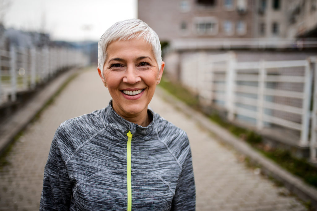 Older athletic woman with dental implants smiling outside