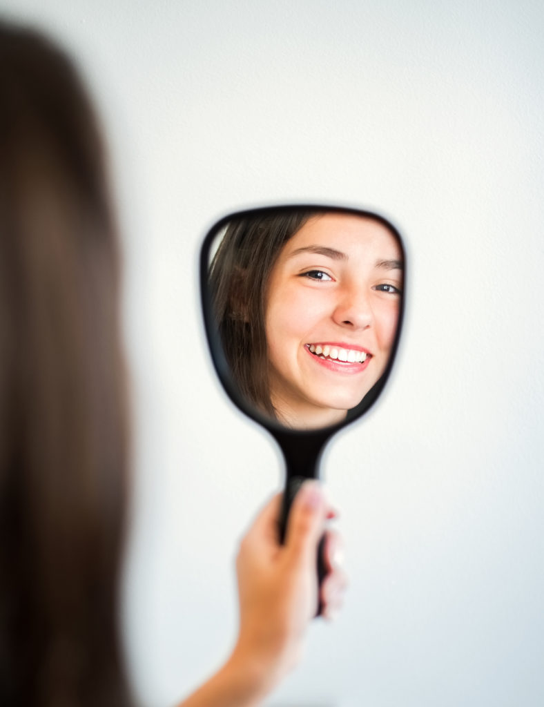 Reflection in the hand mirror of a smiling woman with beautiful teeth