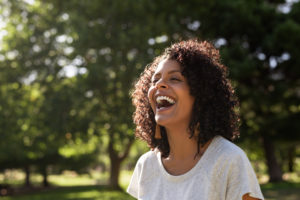 A woman is outside on a sunny day laughing widely