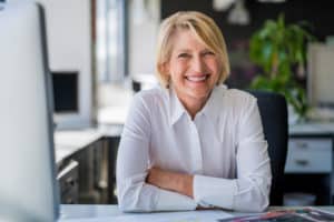 office worker smiling at her desk with her arms crossed after getting tooth extraction