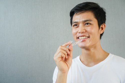 Asian guy holding an Invisalign and smiling
