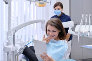 middle aged woman with doctor dentist looking in mirror at teeth